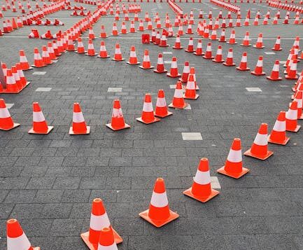 Aerial view of traffic cones arranged on a paved surface, forming a complex pattern.